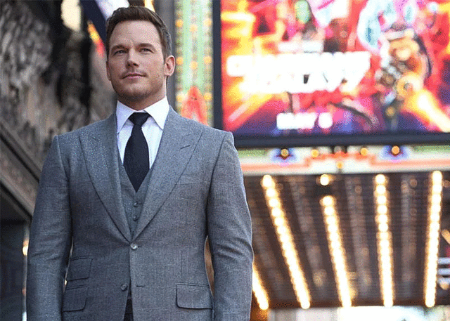 Man in tailored suit stands by theater marquee.