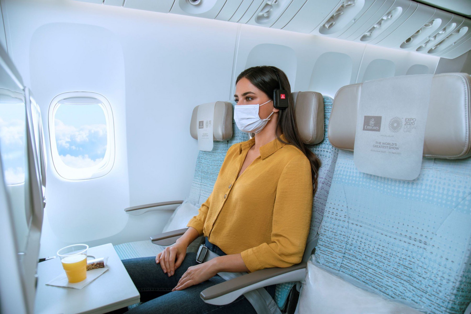 Masked woman enjoys drink on Emirates flight.