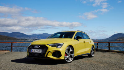 A yellow Audi hatchback parked by water.