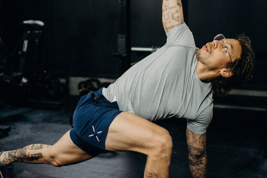 Tattooed person in gym gear stretches before lifting.