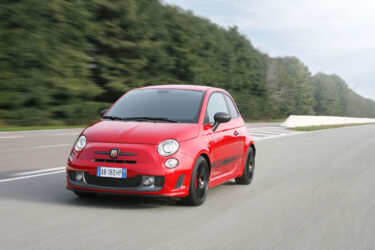 Red hatchback speeds past trees under Australia's sky.