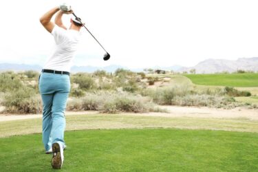 Golfer swings stylishly on fairway under clear sky.