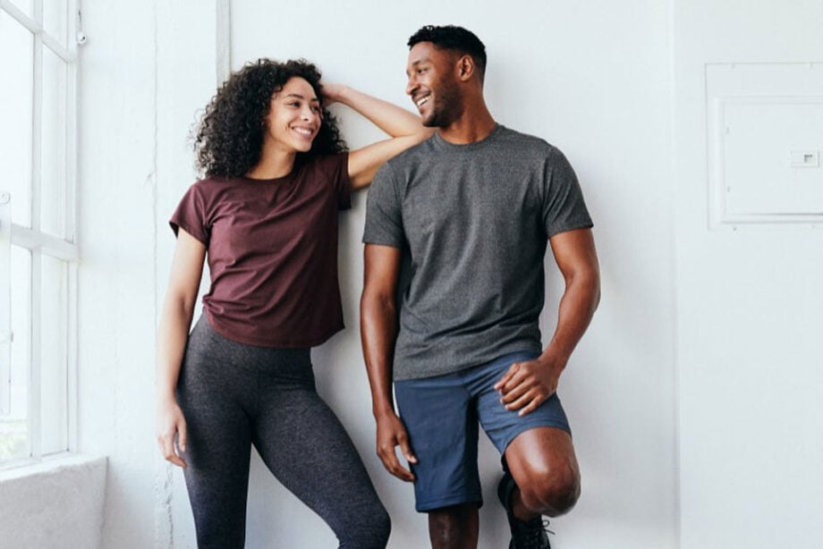 Couple smiles indoors wearing workout clothes.