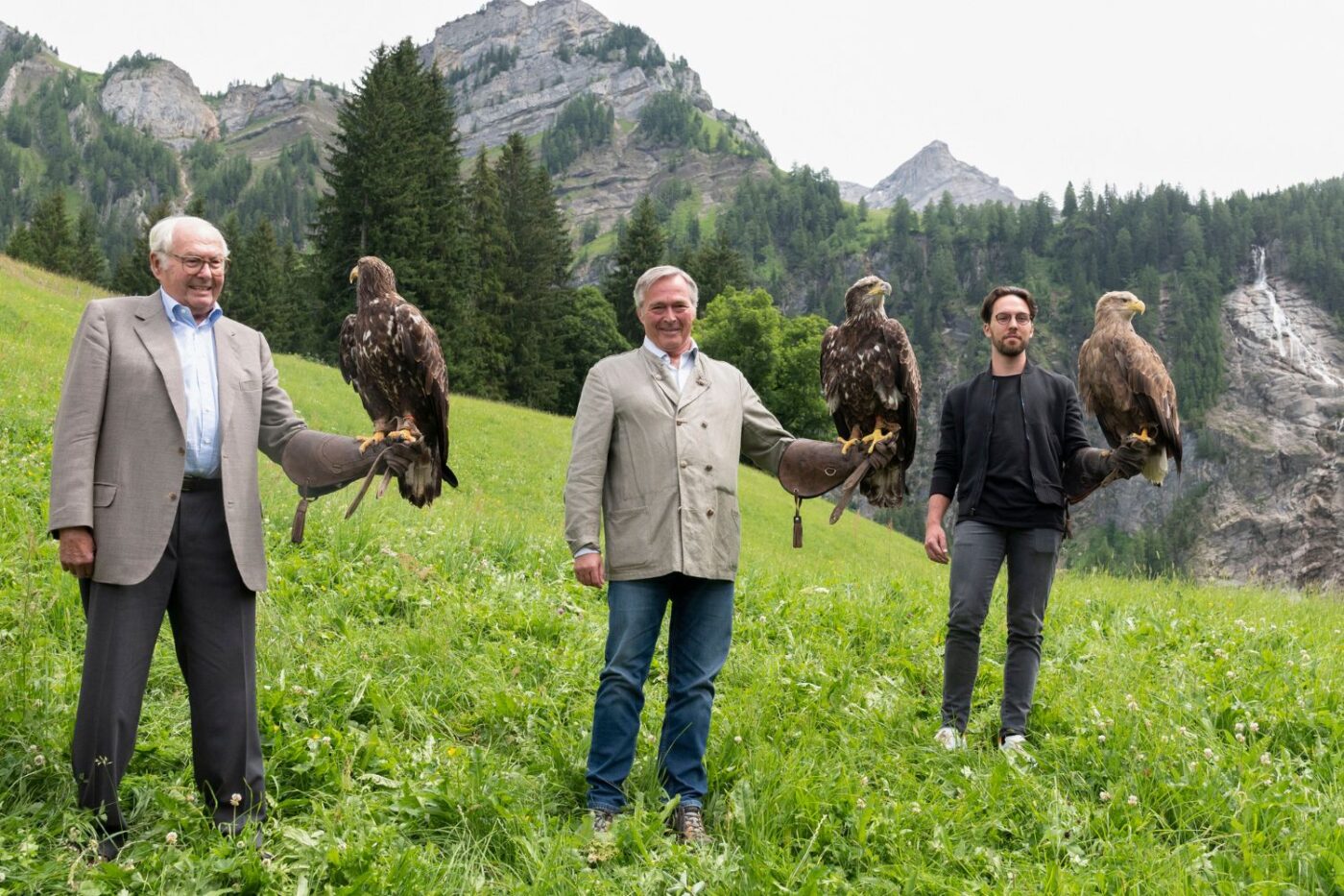 Three men with eagles outdoors.