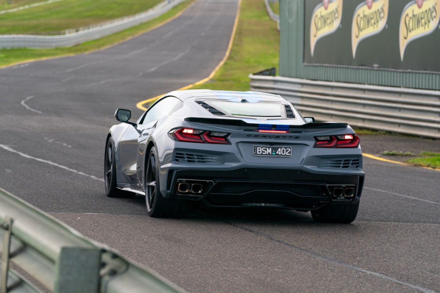 Silver Corvette races in Melbourne by Schweppes billboard.