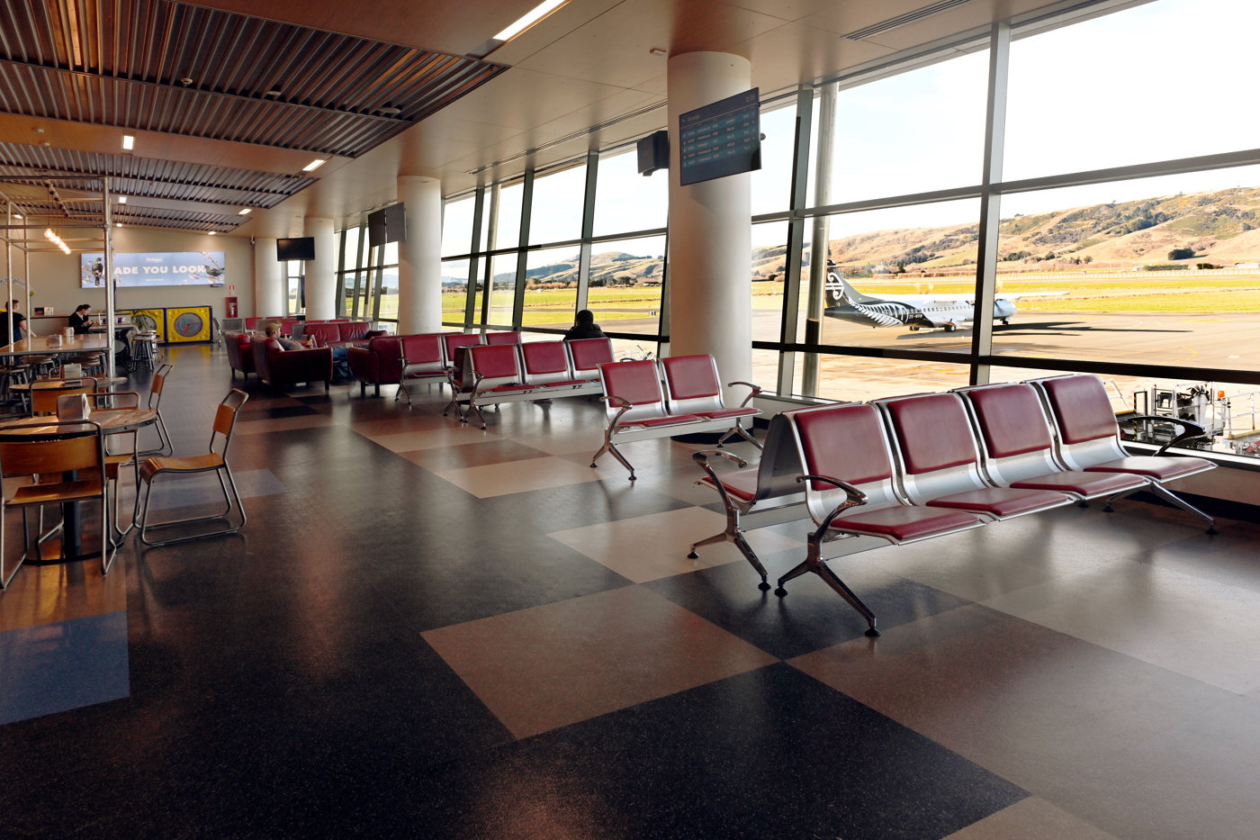 New Zealand airport terminal: empty seats, parked airplane.