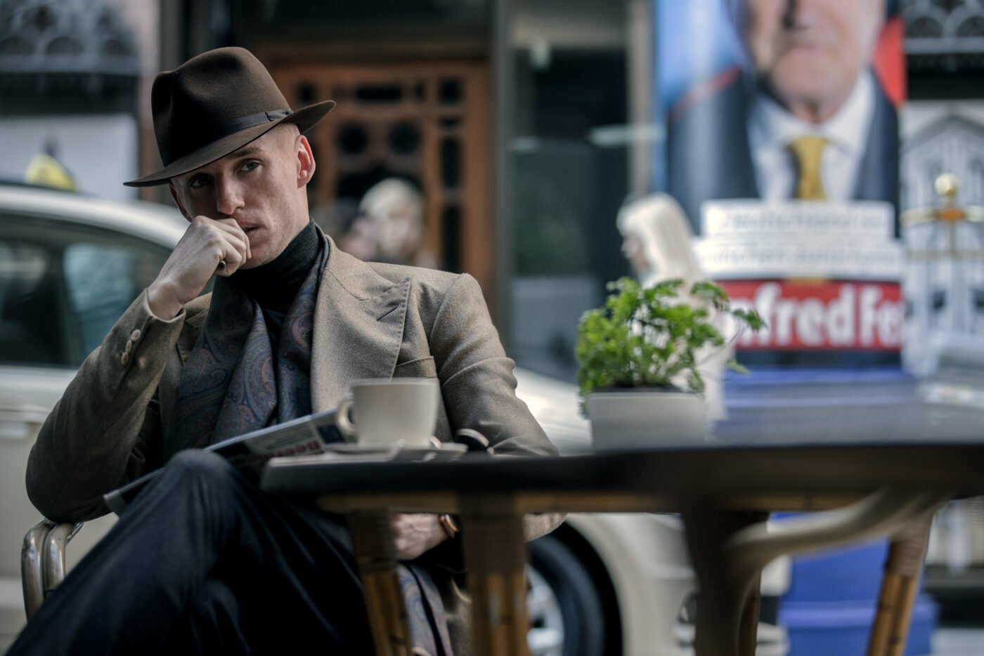 Eddie Redmayne at café with newspaper in Day of The Jackal 