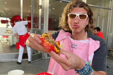 Person with sunglasses holds burger at restaurant.