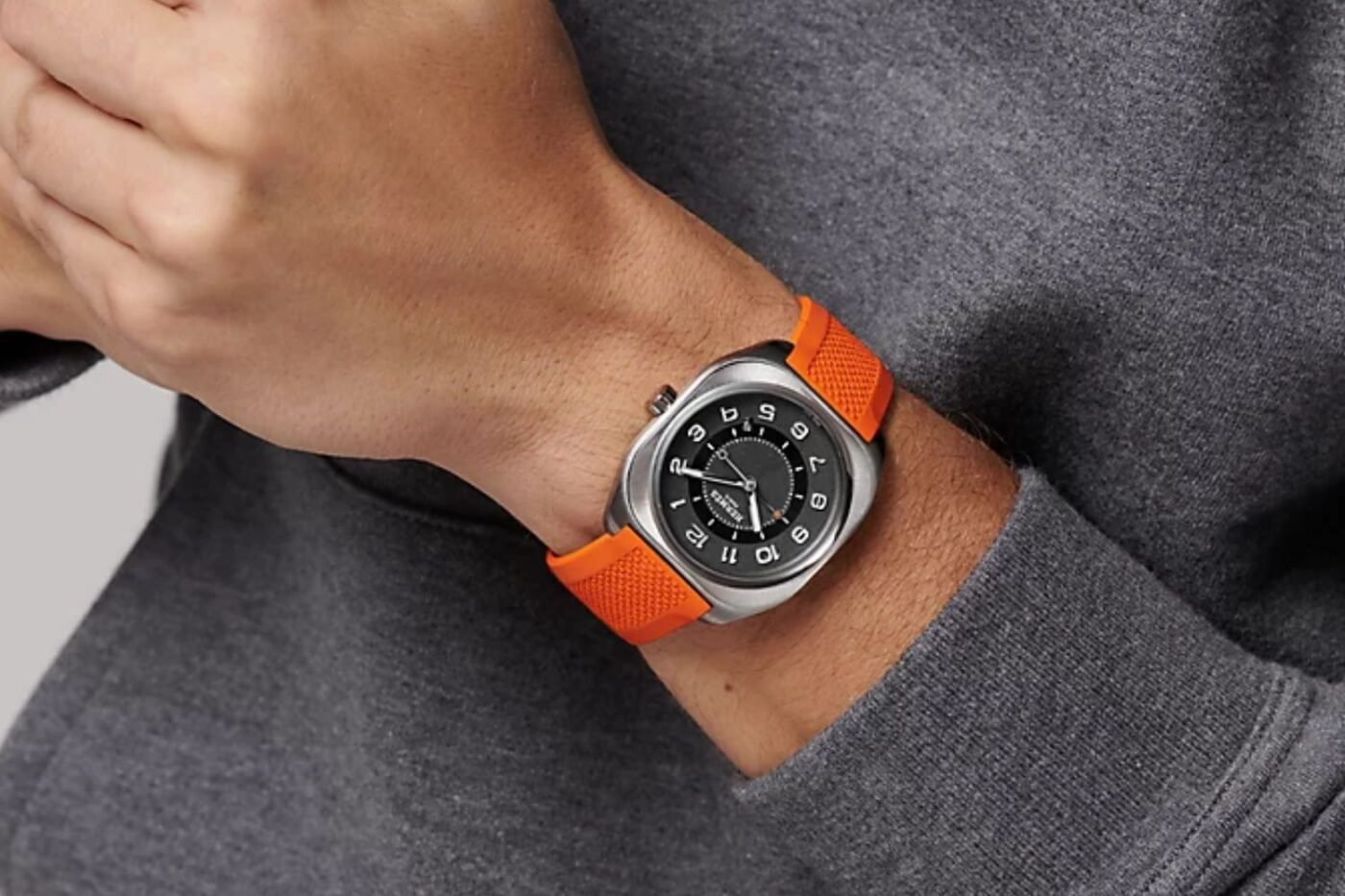 Person models Rise watch: silver face, orange strap.