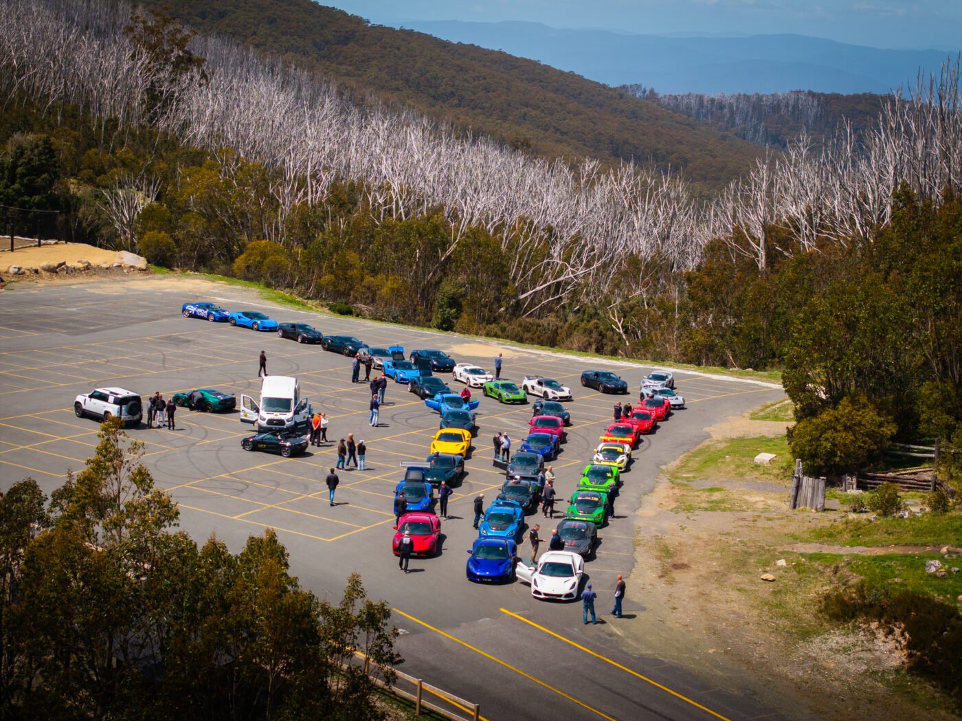 Sports cars parked, people nearby, mountain backdrop.