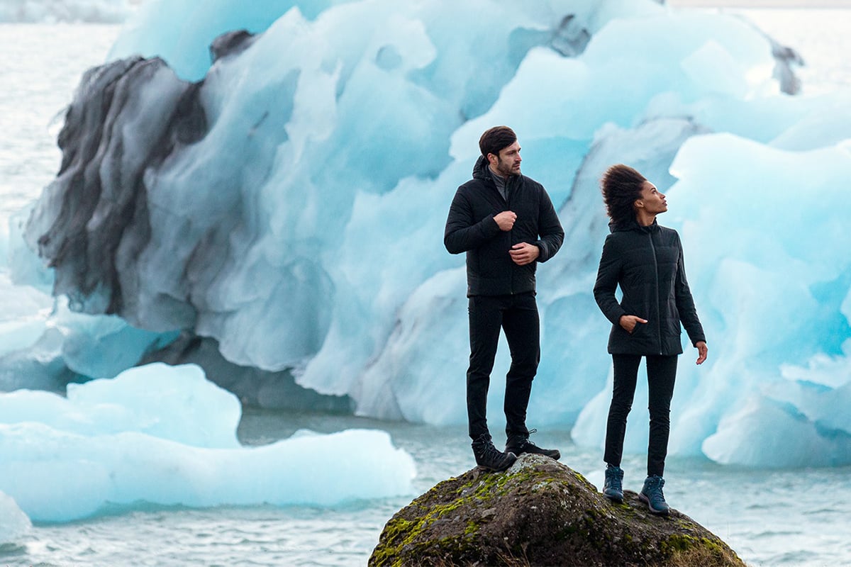 Two in black jackets against icy backdrop.