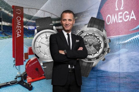 Man in suit before OMEGA watches and stadium.