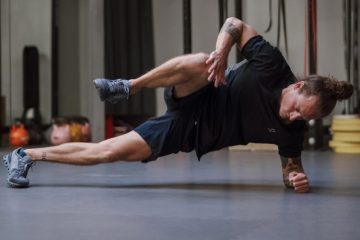 Tattooed athlete side planks at gym.