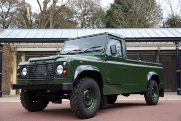 Green Land Rover Defender parked on red asphalt.