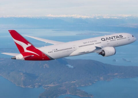 Qantas Dreamliner soars over scenic landscape.