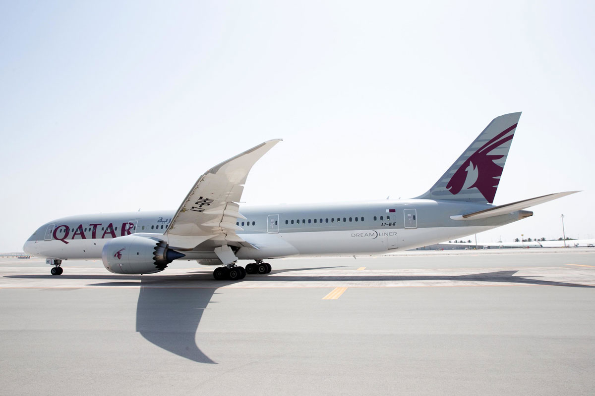 Qatar Airways Dreamliner on runway under clear sky.