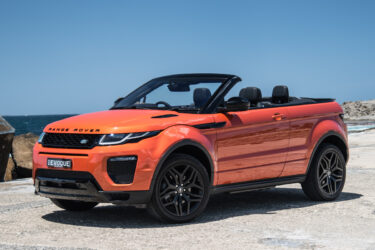 Orange Range Rover Evoque convertible by seaside rocks.