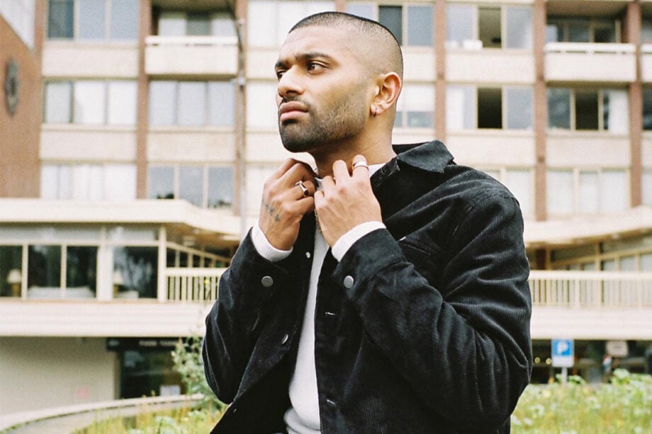 Person adjusts designer jacket outside multi-story building.