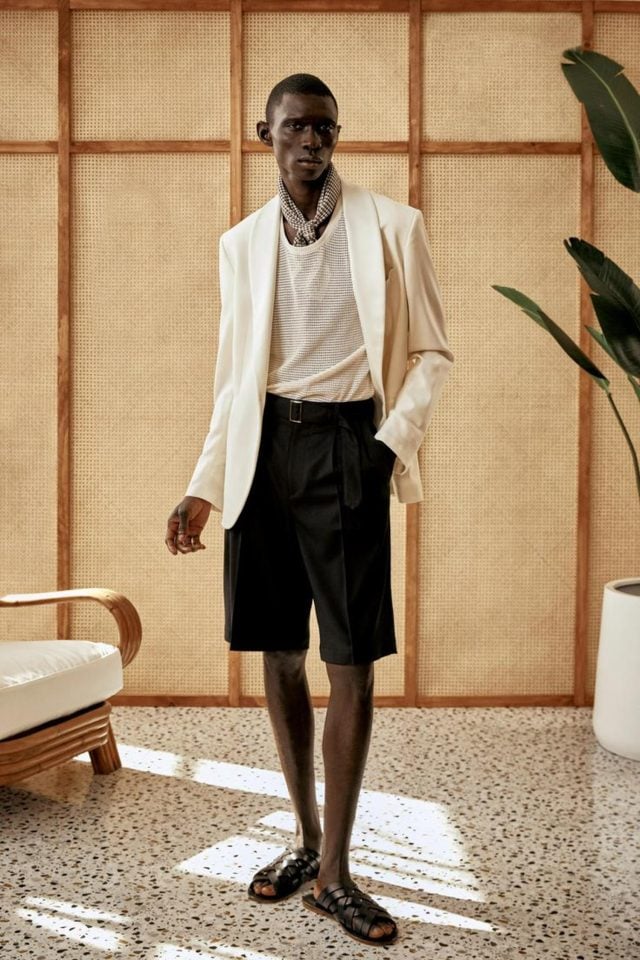 A model wearing white blazer paired with black short and slippers