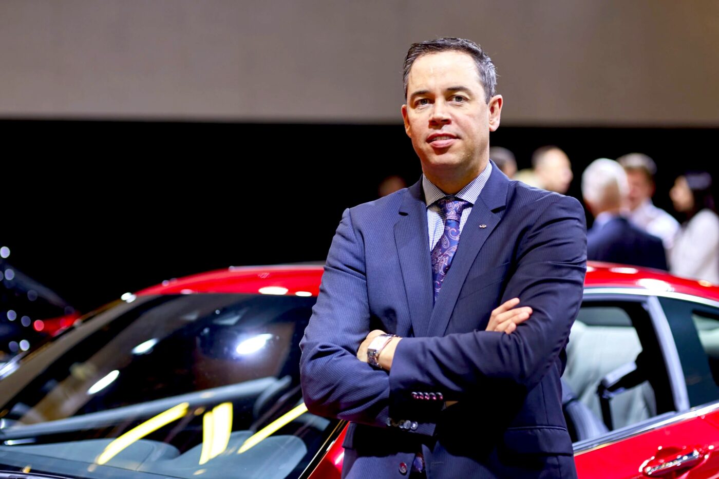 Stephen Lester poses by a red car.