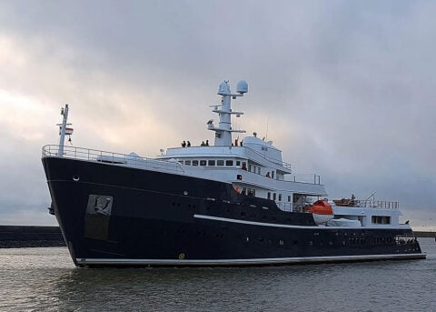 Modern black-hulled yacht sails under cloudy sky.