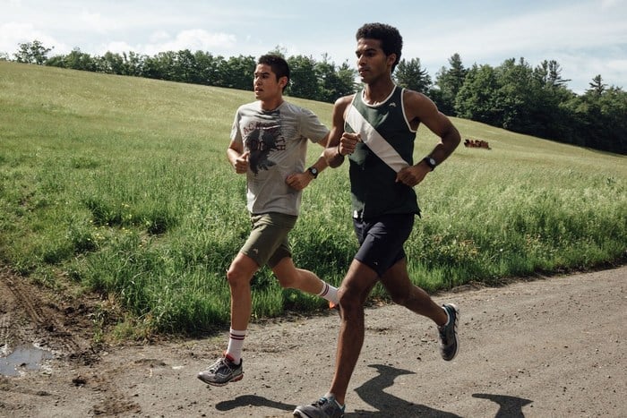 Two men jog beside field.