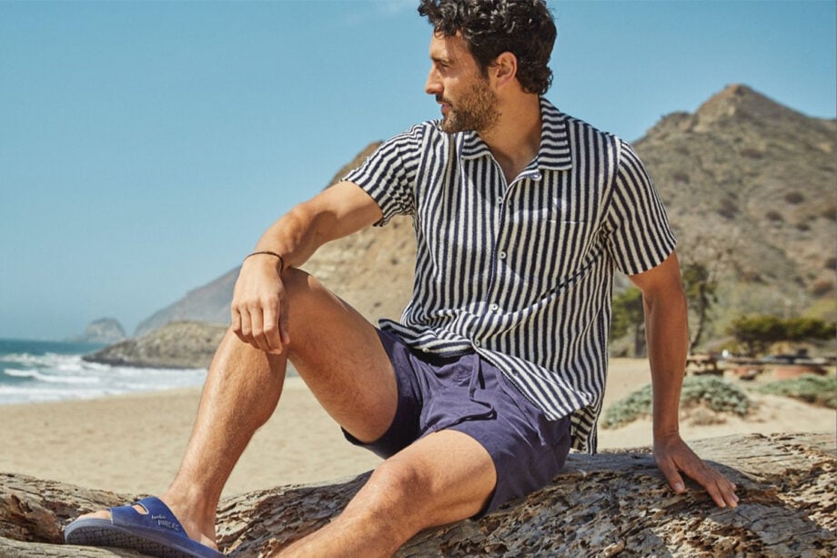 Man in designer attire sits by ocean.