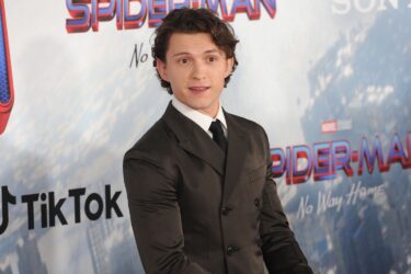 Tom Holland at event with "Spider-Man" backdrop.