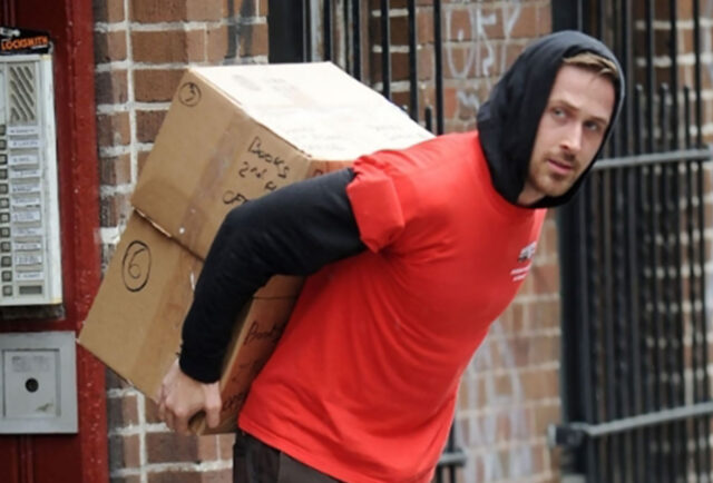 Person in red shirt moves boxes outside building.