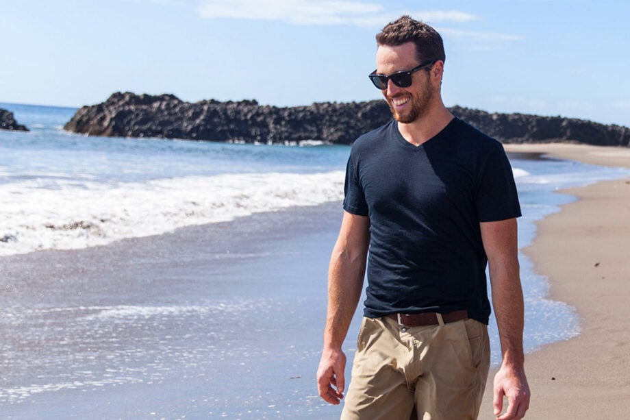 Man strolls beach in designer wear, smiling.