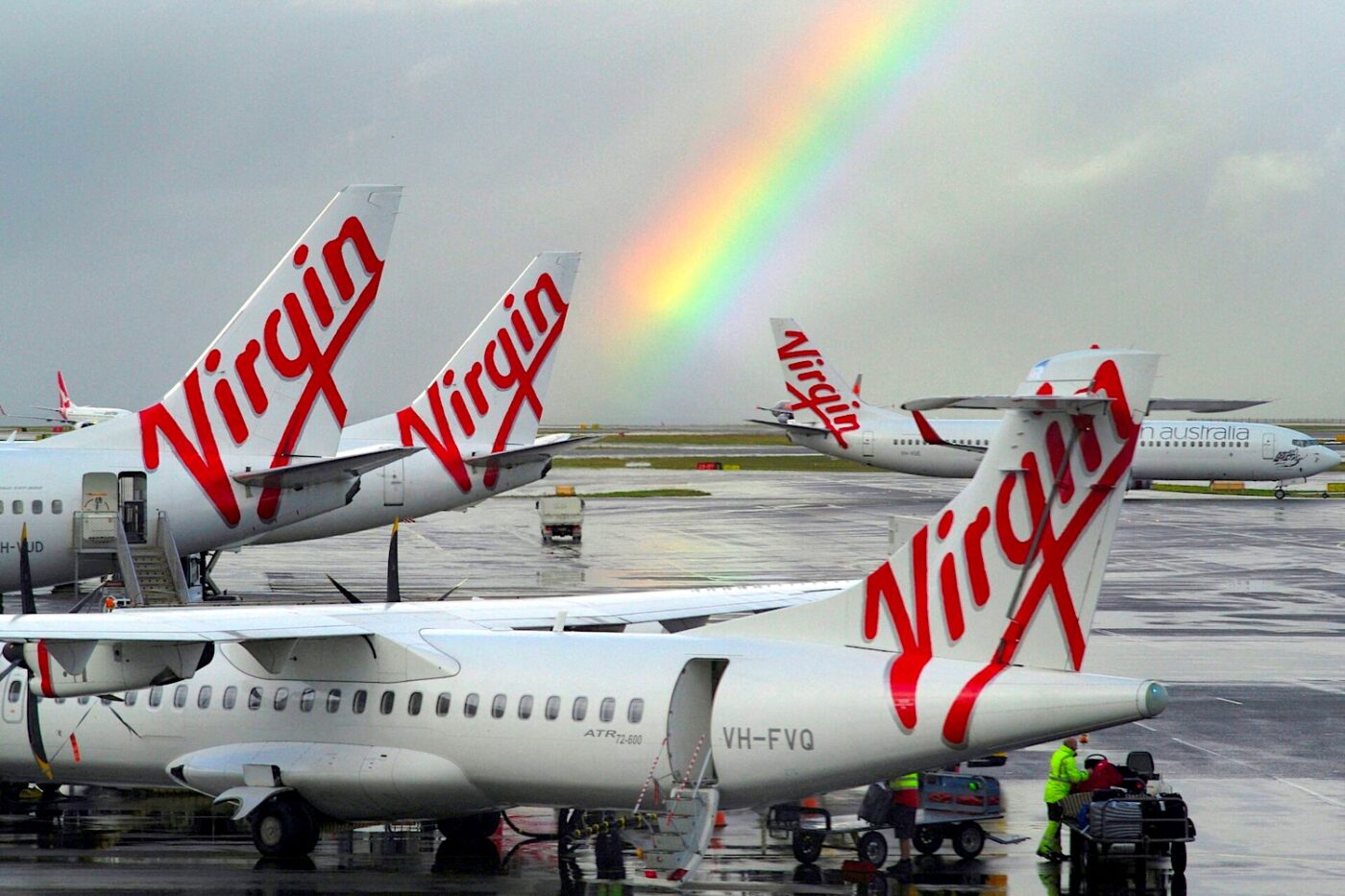 Virgin planes parked under rainbow at airport.