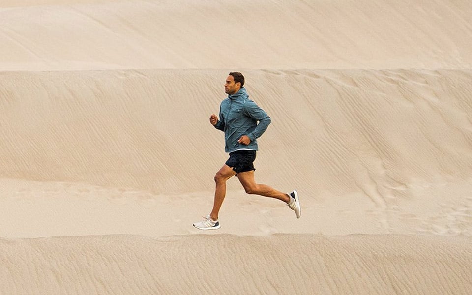 A person runs across sand dunes wearing popular athletic brands.