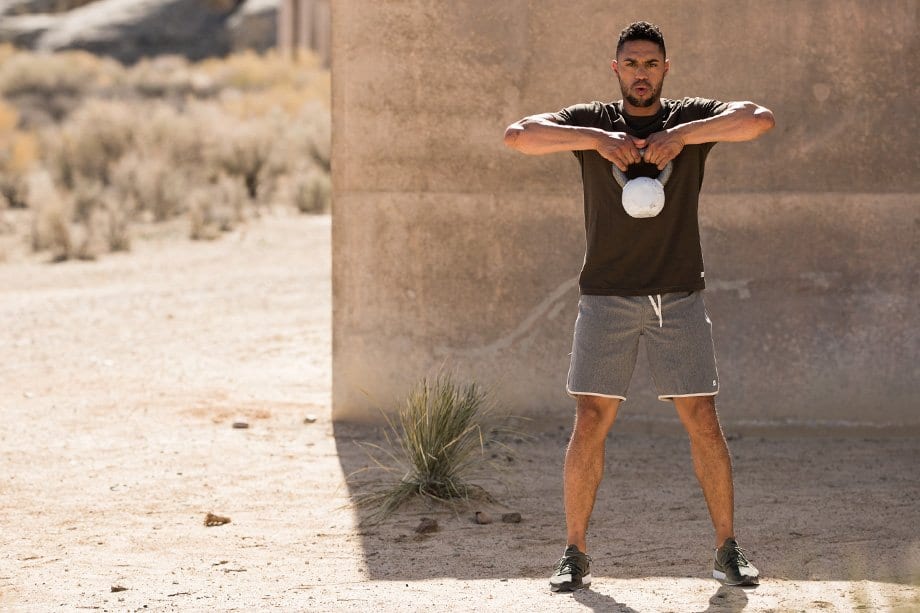 Man lifting kettlebell outdoors, gymwear.