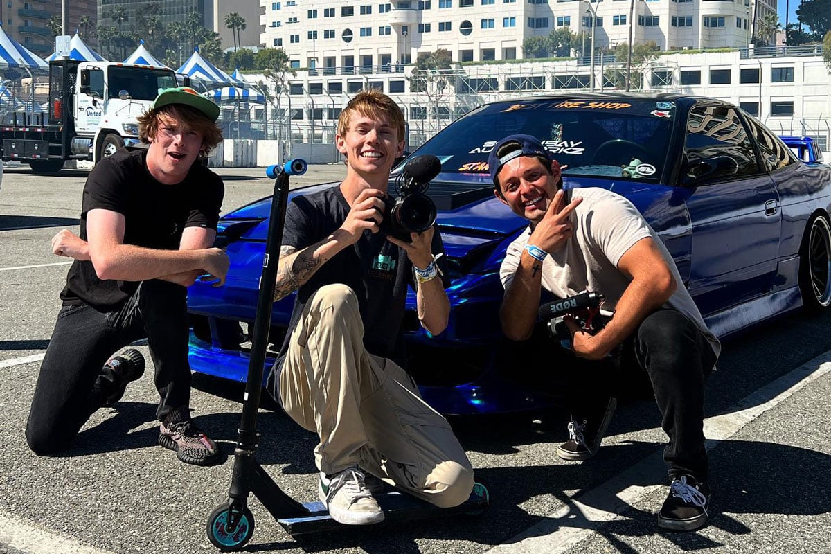 Influencers pose with blue sports car outdoors.