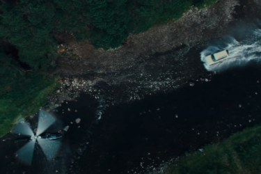 Toyota Prado splashes through river, helicopter nearby.