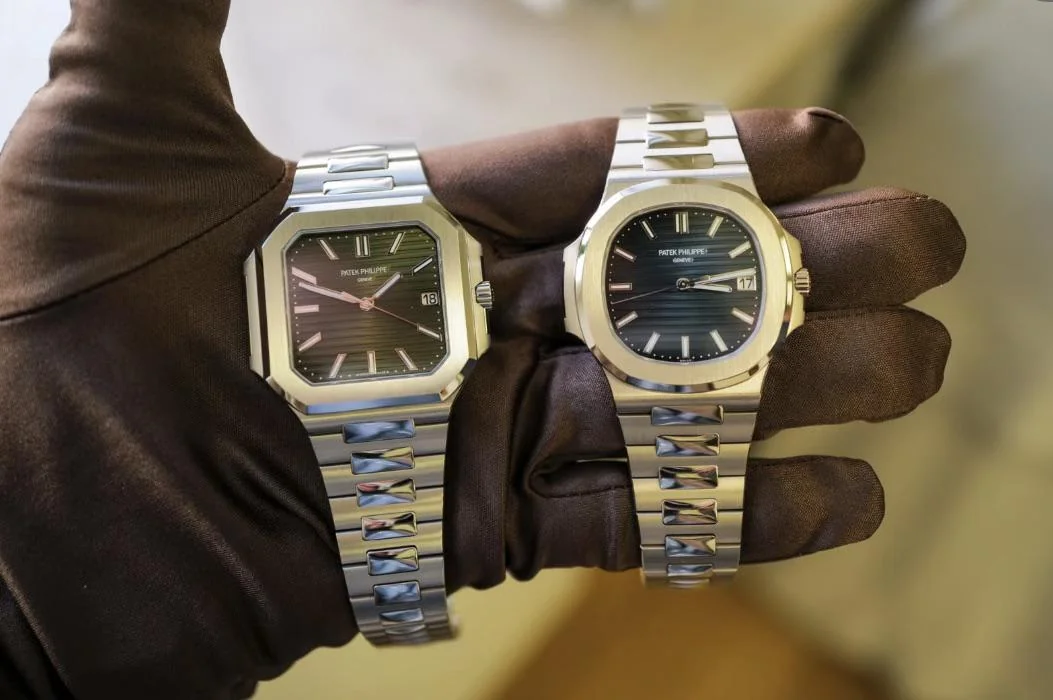 Gloved hand holds two Patek Philippe watches.