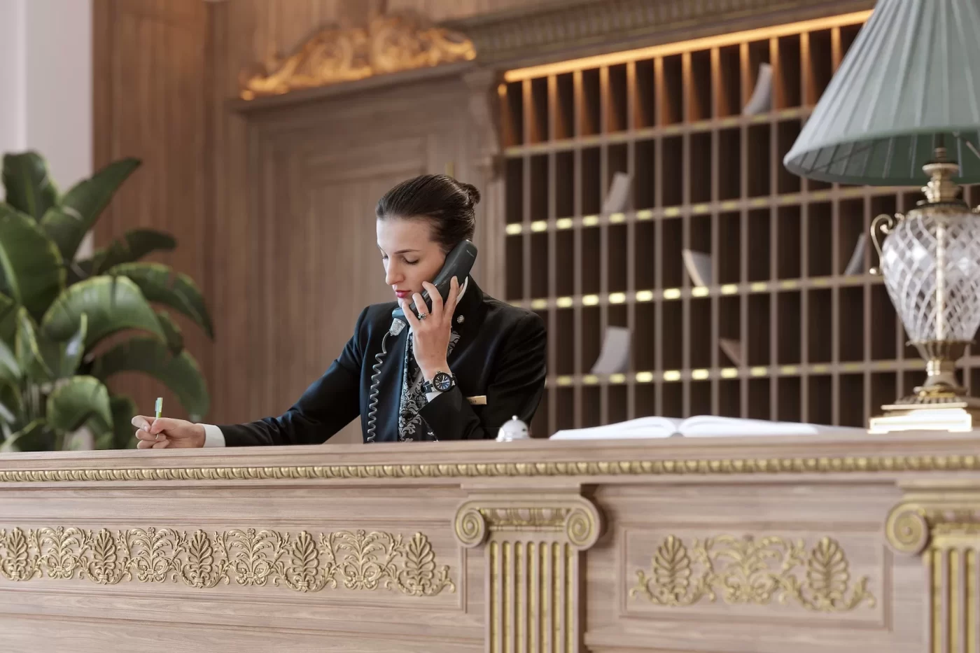 Receptionist discusses booking; ornate decor, mail slots.