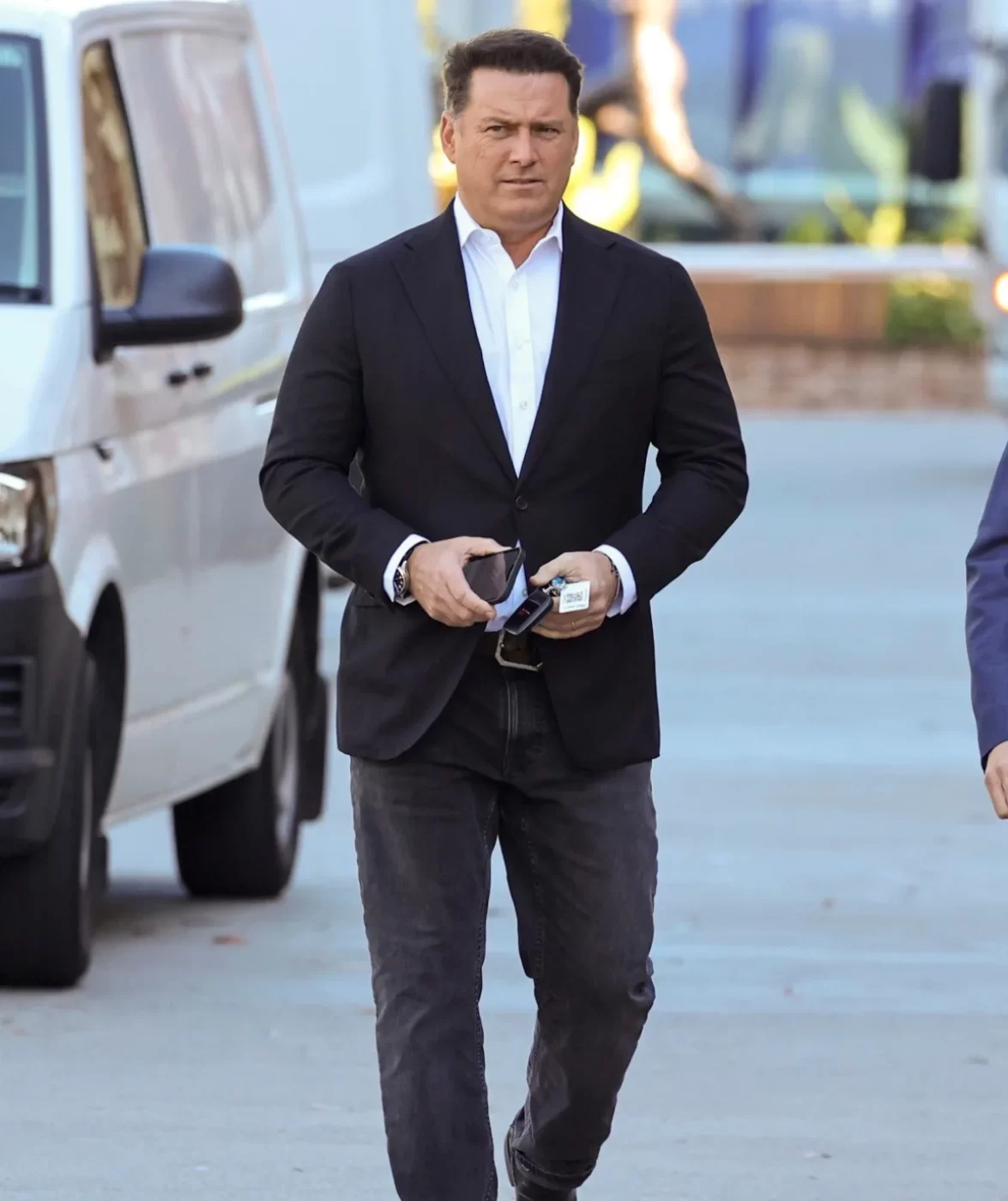 Man in black holds Rolex, walks sidewalk.